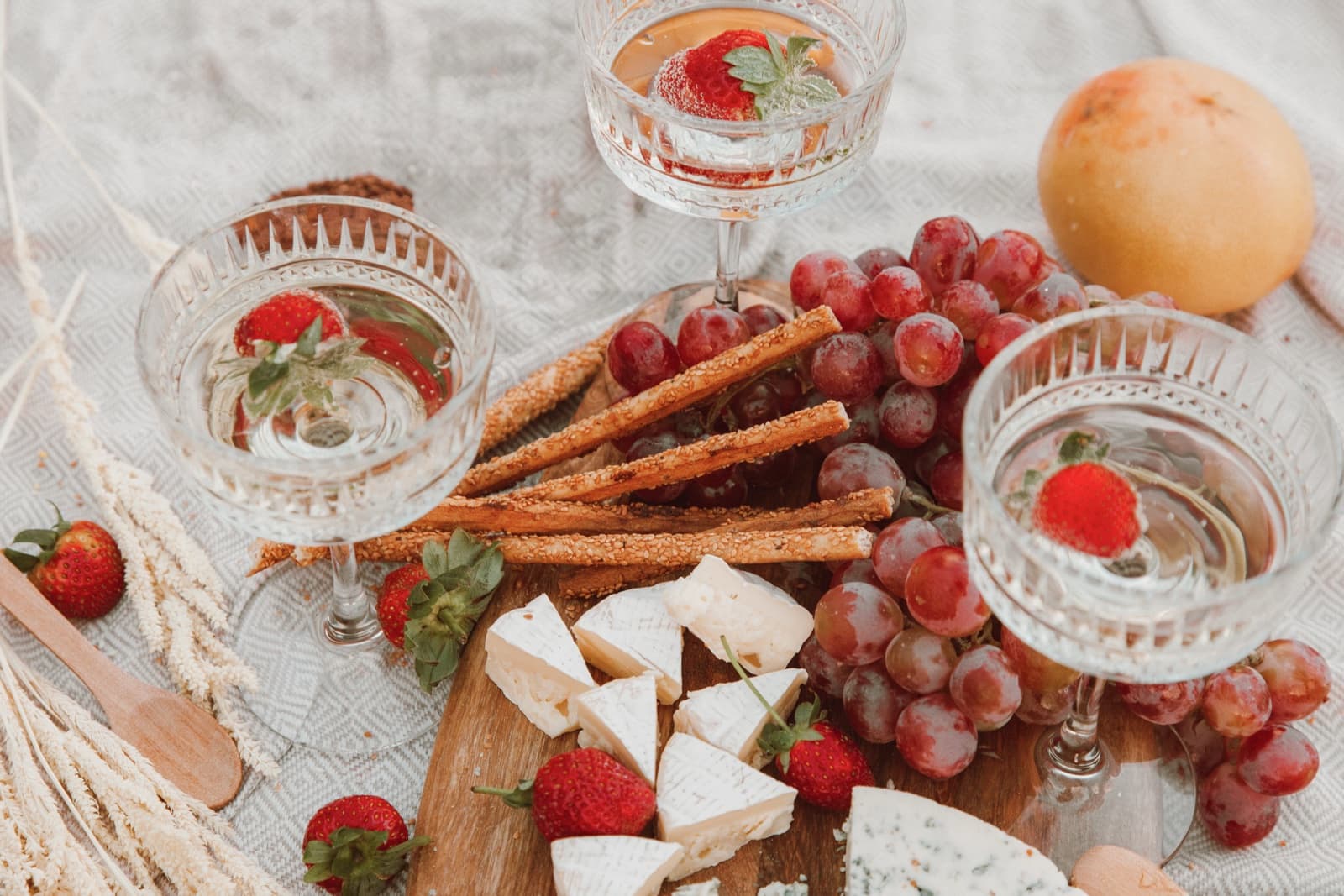Coupe glasses with strawberries beside a cheese board, grissini and grapes on linen