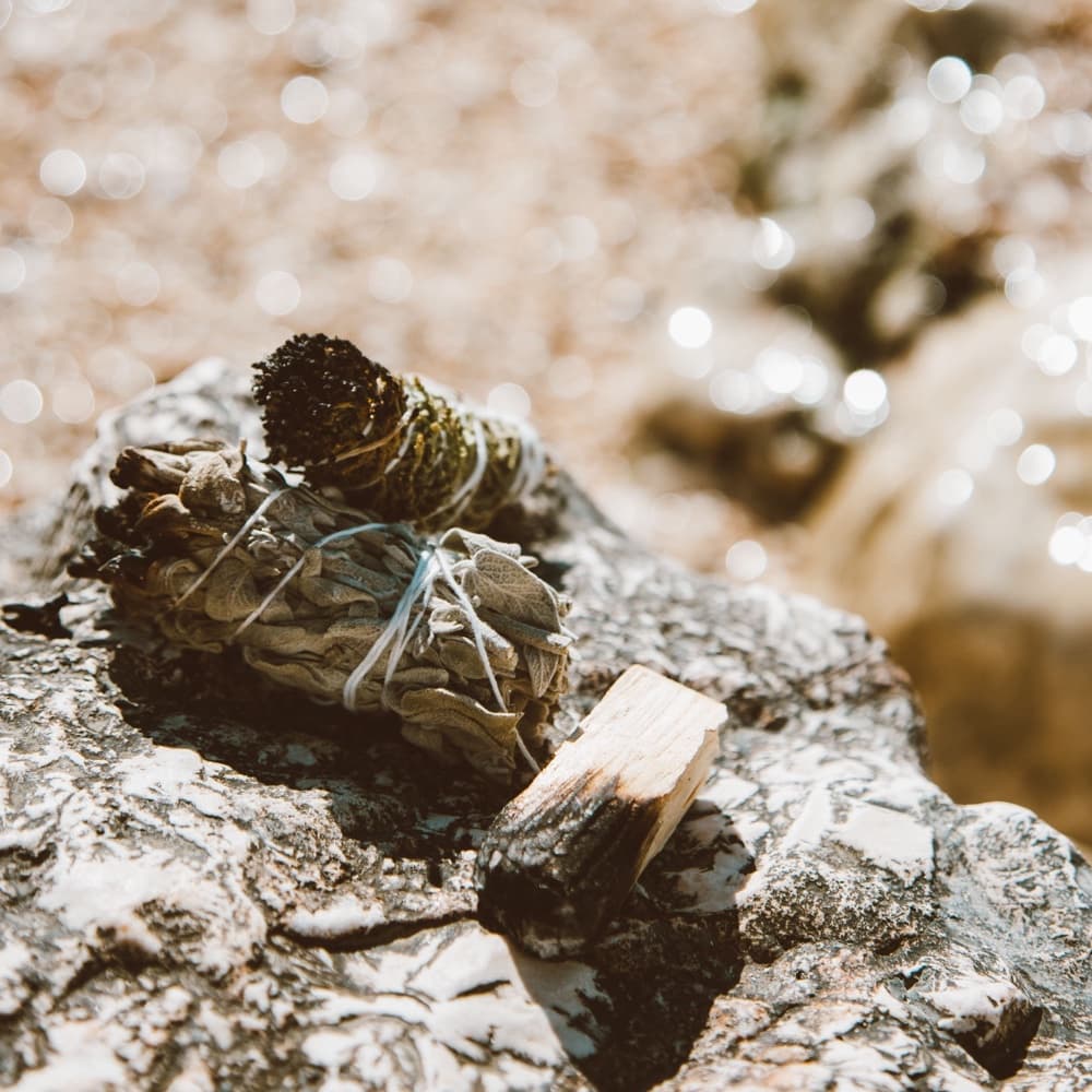 A bundle of dried sage and a piece of palo santo resting on pale rock