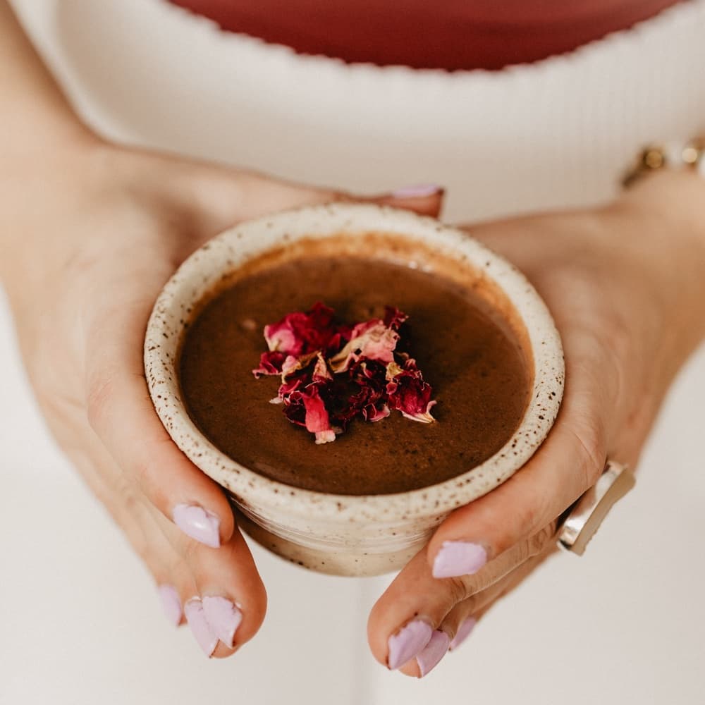 Hands cradling a speckled ceramic cup of cacao topped with dried rose petals