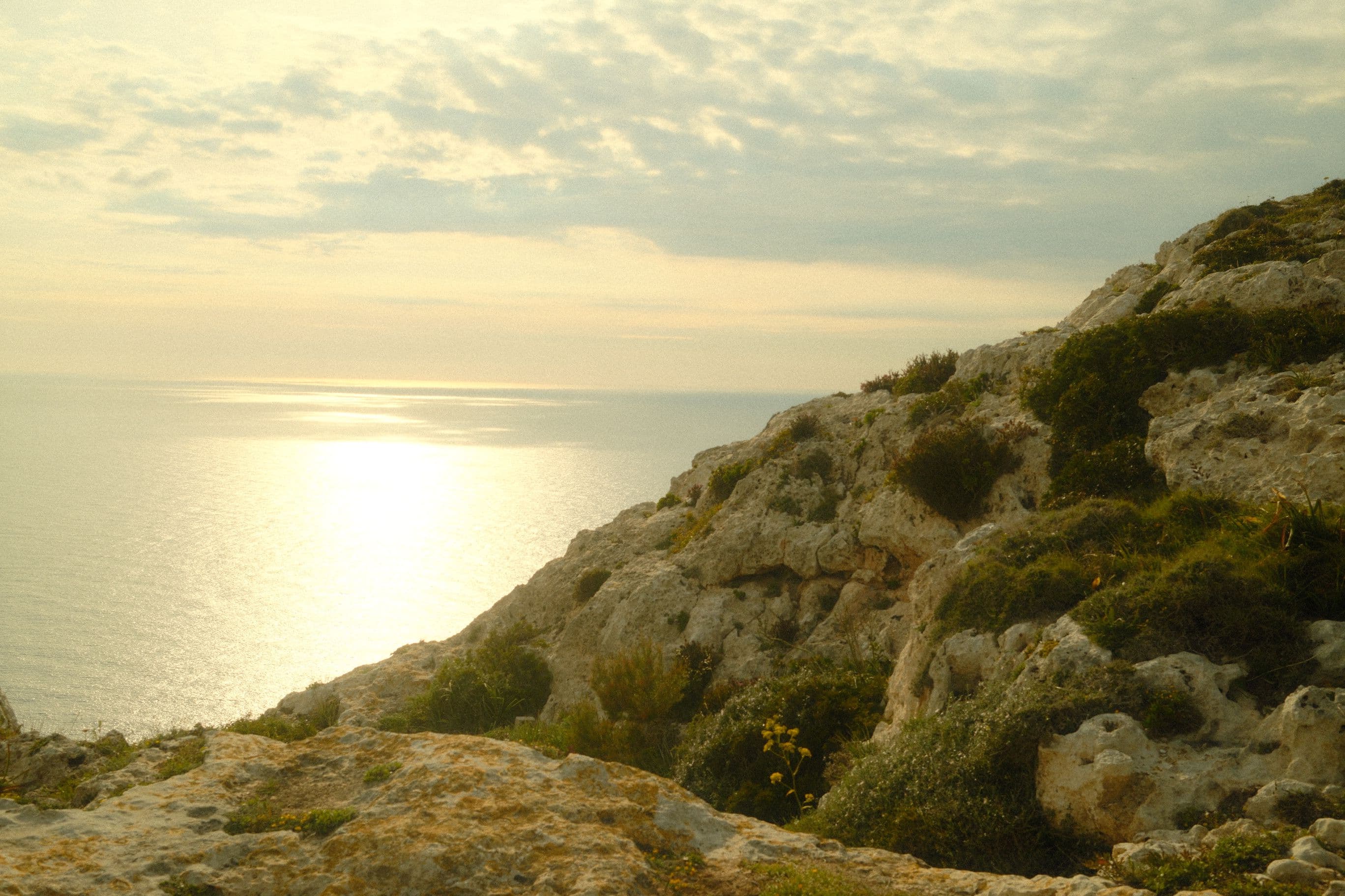 Limestone clifftop above the sea, low sun laying a path of light across the water
