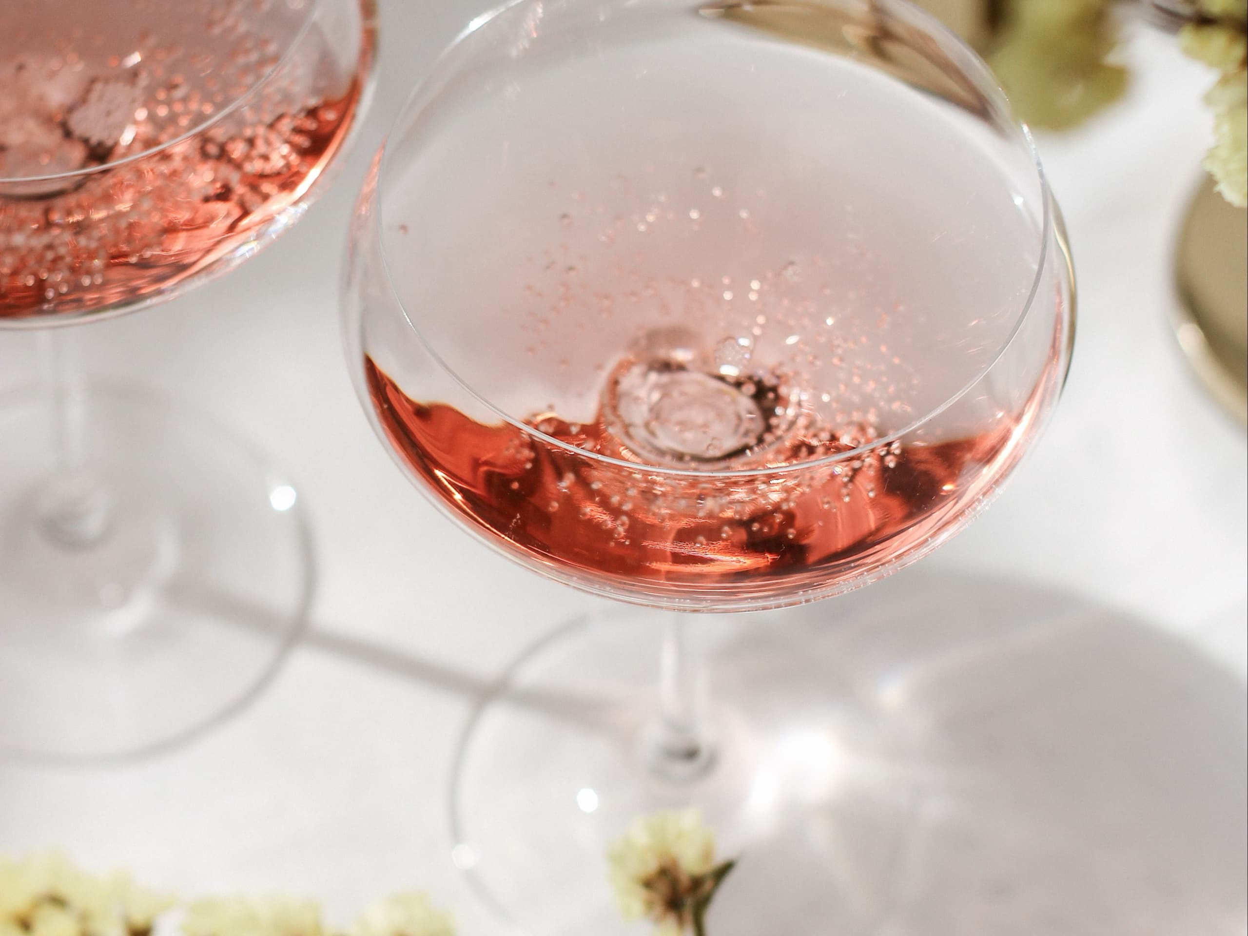 Two coupe glasses of rosé on white cloth, gypsophila and hard sunlight