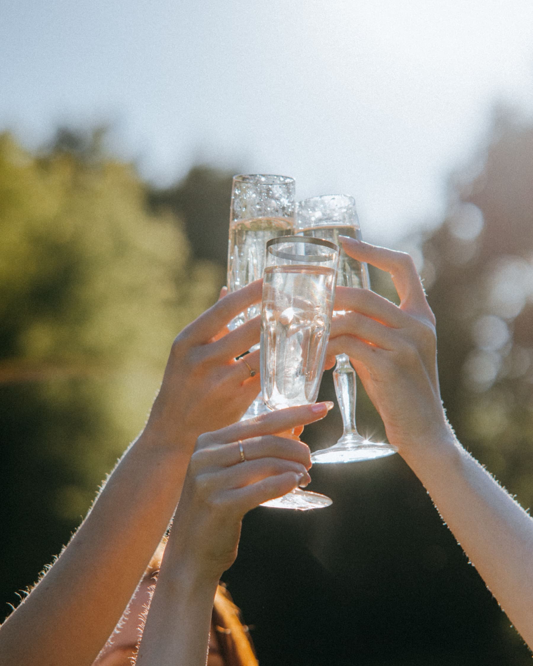 Hands raising champagne glasses against a bright sky