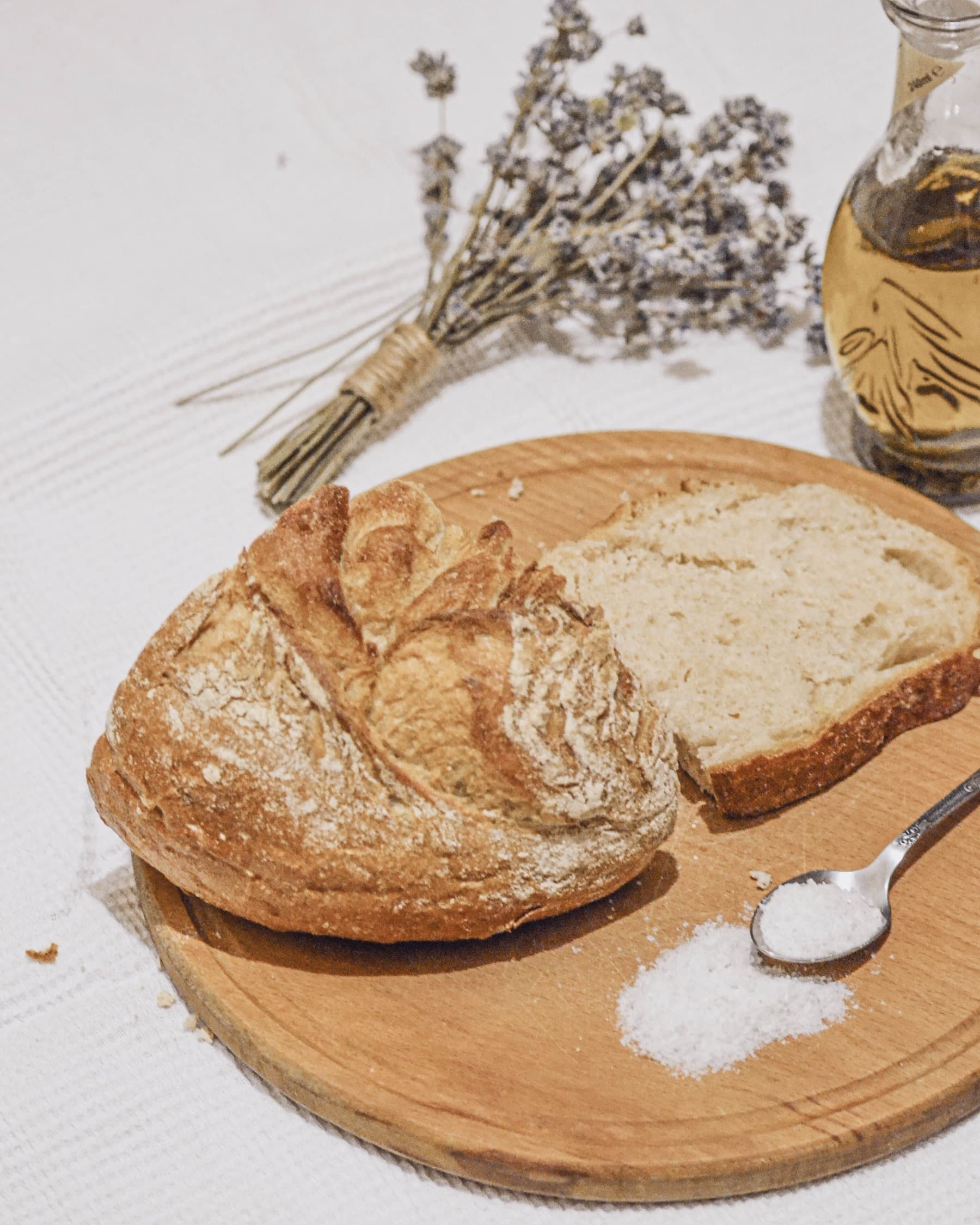 A round board with a rustic loaf, a cut slice, a spoon of salt and dried lavender