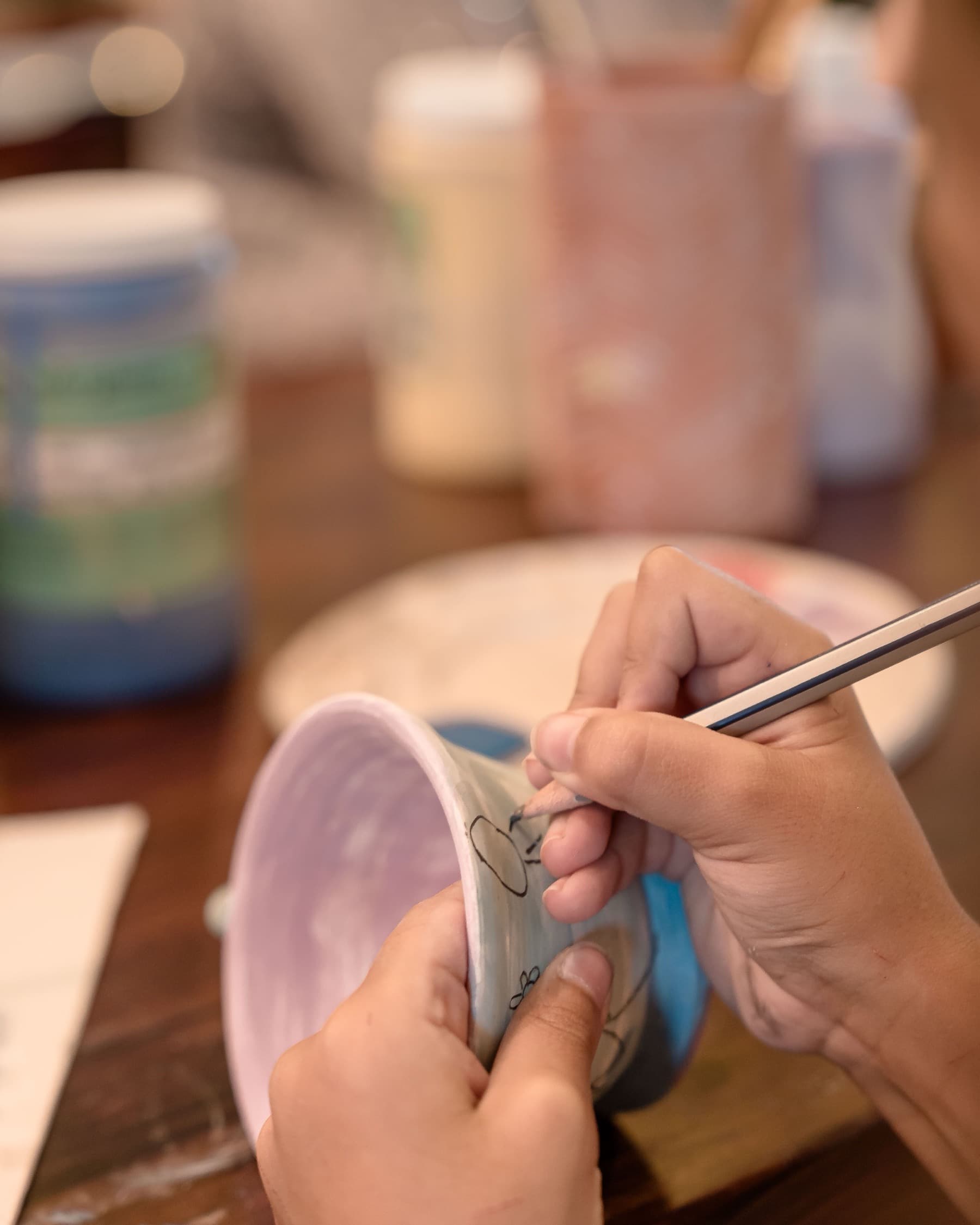Hands painting a pattern onto a ceramic bowl at a workshop table